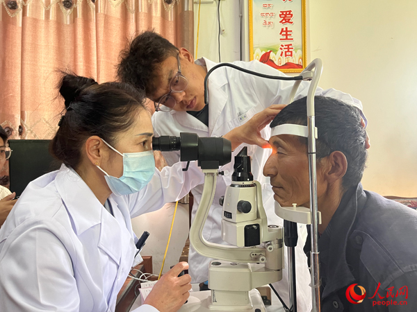 王紅英（左）和團(tuán)隊成員為達(dá)熱村村民檢查眼睛。人民網(wǎng)記者 杜燕飛攝