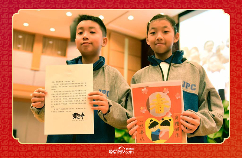 圖為香港“少年警訊”成員郭宏晞（左）展示習(xí)主席回信、羅顥凝（右）展示送給習(xí)主席的賀卡并合影。