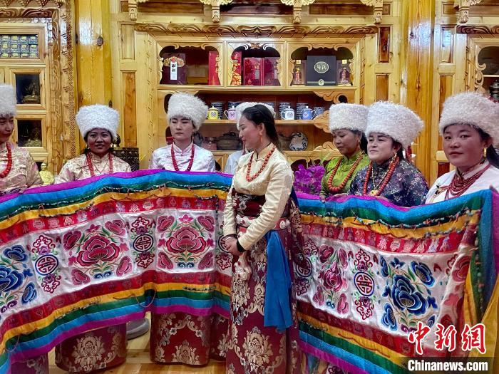 圖為女性展示村民自發(fā)繡制的“百米五彩哈達(dá)”。　李玉峰 攝